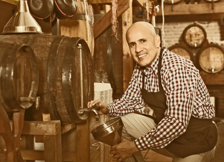 cheerful man 50-55 years old wearing apron holding wine in wine houseの写真素材