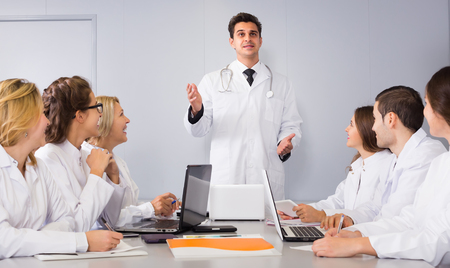 Group of young positive scientists in white overalls at the conference of research workの写真素材