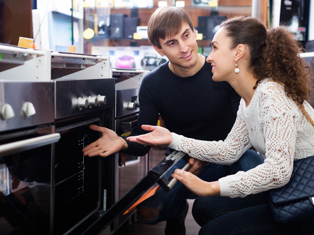Happy young couple choosing kitchen oven in store and smilingの写真素材