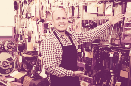 Elderly seller posing near electric compressor in household storeの写真素材