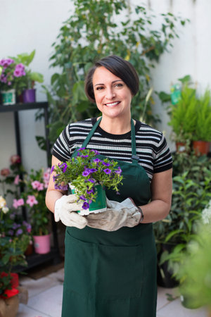 Glad friendly pleasant  woman florist smiling among the potted plants in the floral shopの写真素材