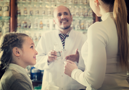 Female customer with a kid and joyful male pharmacist in white coat at the counter in pharmacyの写真素材