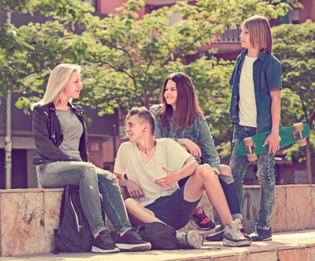 Portrait of four cheerful smiling teenage friends sitting and chatting outdoors in town