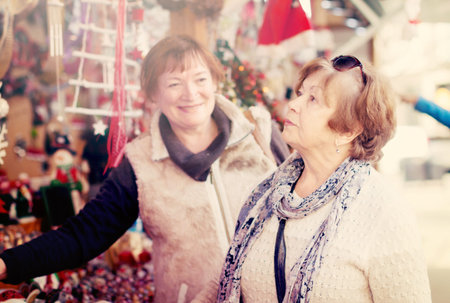 Two senior women considering decorations at counter of Christmas marketの写真素材