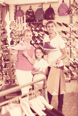 smiling young parents with boy choosing new sport shoes in sport shopの写真素材