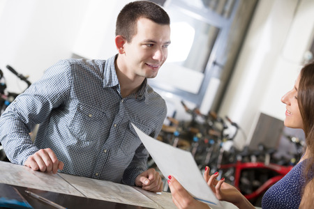 russian female employee helping adult guy to select bike at rental agencyの写真素材