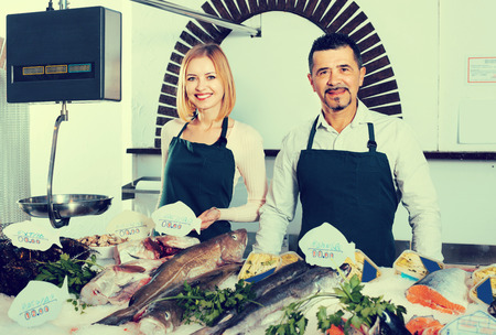 Portrait of two smiling sellers in aprons in fish section of supermarketの写真素材