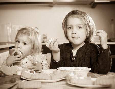 Two little sisters eating cream desserts at home kitchenの写真素材