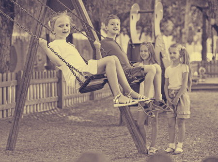 View on happy cheerful  children swinging together on children's playground in townの写真素材