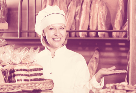 Cheerful mature woman selling fresh pastry and baguettes in local bakeryの写真素材
