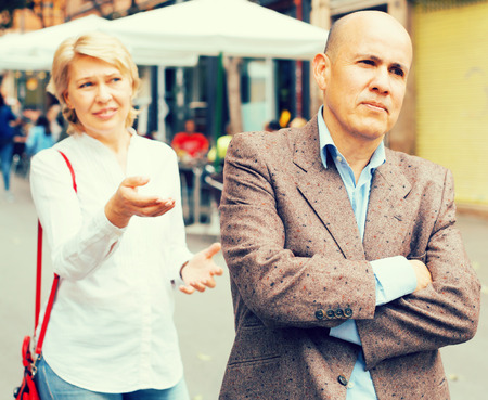 Portrait of annoyed mature man standing away from arguing woman outdoorsの写真素材