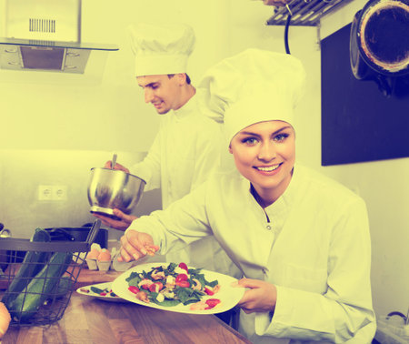 Young woman chef serving fresh salad at restaurant's kitchen