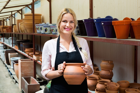 Portrait of positive smiling  woman pottery worker with ceramic crockery in hands in studioの写真素材