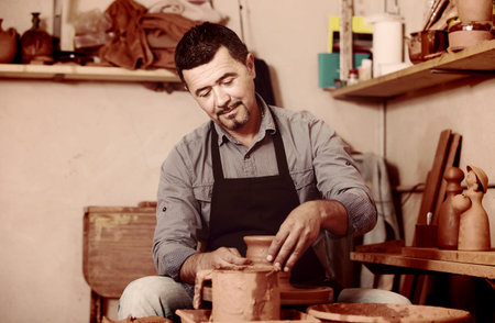positive artisan man creating ceramic piece on spinning pottery wheel in workshop