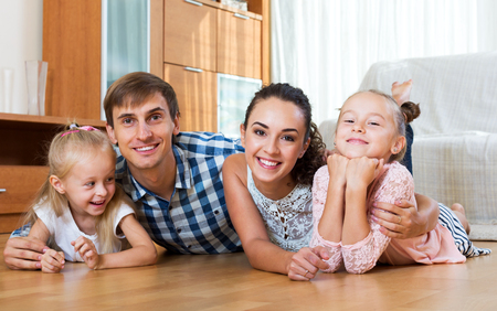 Smiling young couple with two little girls relaxing at homeの写真素材
