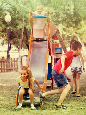 smiling playful boy and girls in elementary school age having fun on slide  at playground. Selective focusの写真素材