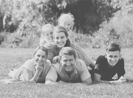 Portrait of big happy family with parents and four children lying together on green lawn outdoorsの写真素材