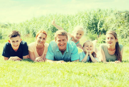 happy man and woman with four children lying on the grass in park on summer dayの写真素材