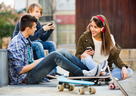 Smiling cheerful teens playing on smarthphones and listening to musicの写真素材