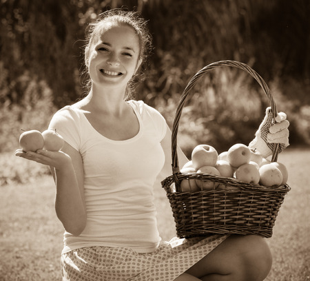 Smiling young woman with basket of apples in the gardenの写真素材