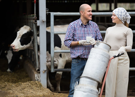 Portrait of two cheerful farmers holding a trolley with milk can and chatting on farm