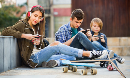 Happy smiling teens playing on smarthphones and listening to music