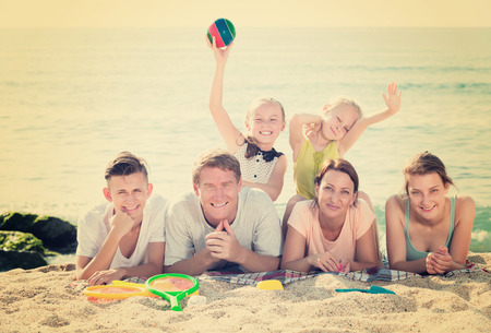 Parents with four children in different ages lying on sand on sea coast in sunny weatherの写真素材
