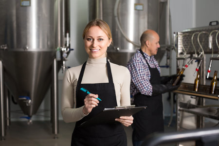 Portrait of joyful young female technologist on beer brewery factory