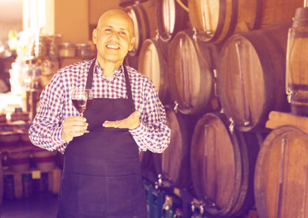 cheerful man wearing apron holding wine in wine house