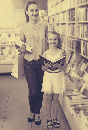 Cheerful glad woman showing open book to girl in school age in book boutiqueの写真素材