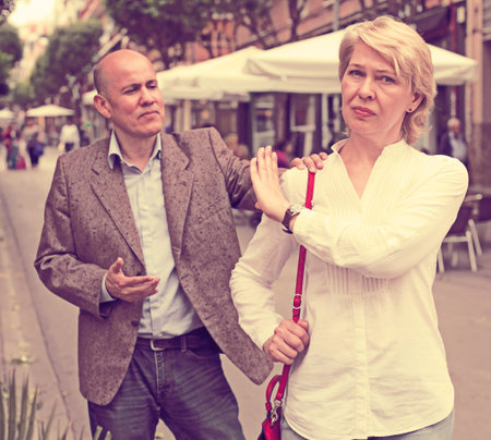 Portrait of annoyed mature woman standing away from arguing man outdoorsの写真素材