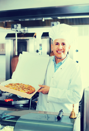 smiling  man chef in uniform holding freshly baked pizza in hands in restaurantの写真素材