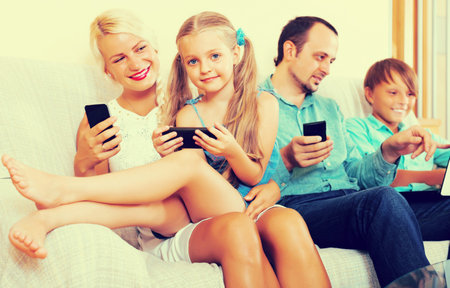 Happy mom, dad and two smiling kids working with smartphones indoors