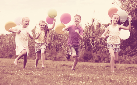 Happy girls and boy running all together  with multicolored balloons in backyardの写真素材