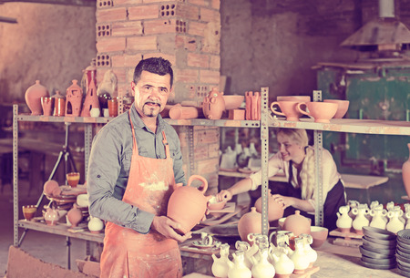 Smiling american man potter holding ceramic vessels in atelierの写真素材