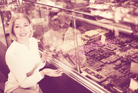 Happy blonde pensioner buying dark and white chocolate filled candiesの写真素材