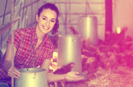 happy young russian  woman farmer holding bucket with chicken forage in hen houseの写真素材