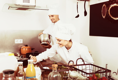 Two adult female and male cooks wearing uniform working on kitchenの写真素材