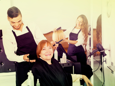 Mature person doing haircut at the hair salon with hairdresser and smilingの写真素材