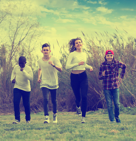 Portrait of four friends running on field in sunny dayの写真素材