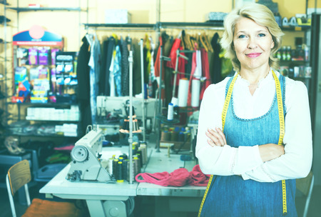 Positive mature woman tailor standing in sewing workshopの写真素材
