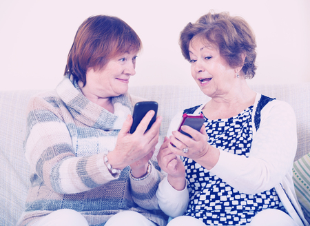 Happy mature women browsing internet on smarthphones indoorの写真素材