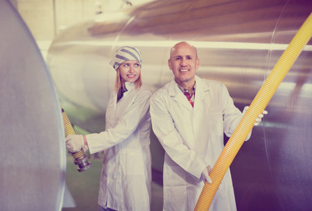 Positive smiling farm employees working in raw milk sector of livestock farm
