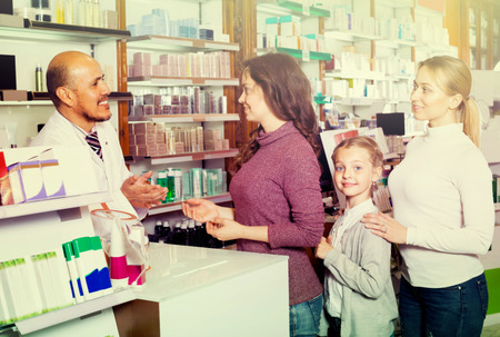 Female customers with a child and smiling male pharmacist in white coat at the counter in pharmacyの写真素材