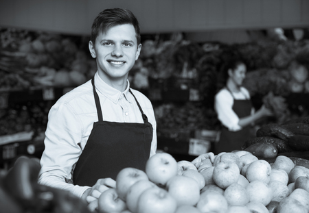 Young male dealer lays out the apples on the counter and smilingの写真素材
