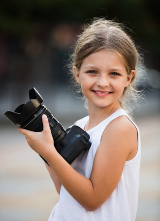 Cheerful smiling girl taking pictures with professional camera outdoors on summer dayの写真素材