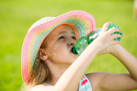 happy girl in elementary school age drinking water from plastic bottle outdoorsの写真素材