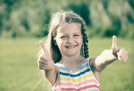 portrait of smiling girl in elementary school age holding thumbs up outdoorsの写真素材