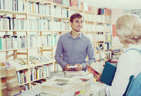 friendly smiling young male seller consulting customer in book shopの写真素材