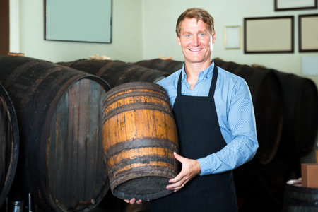 Portrait of male seller wearing uniform carrying wine wood in hands in wine houseの写真素材